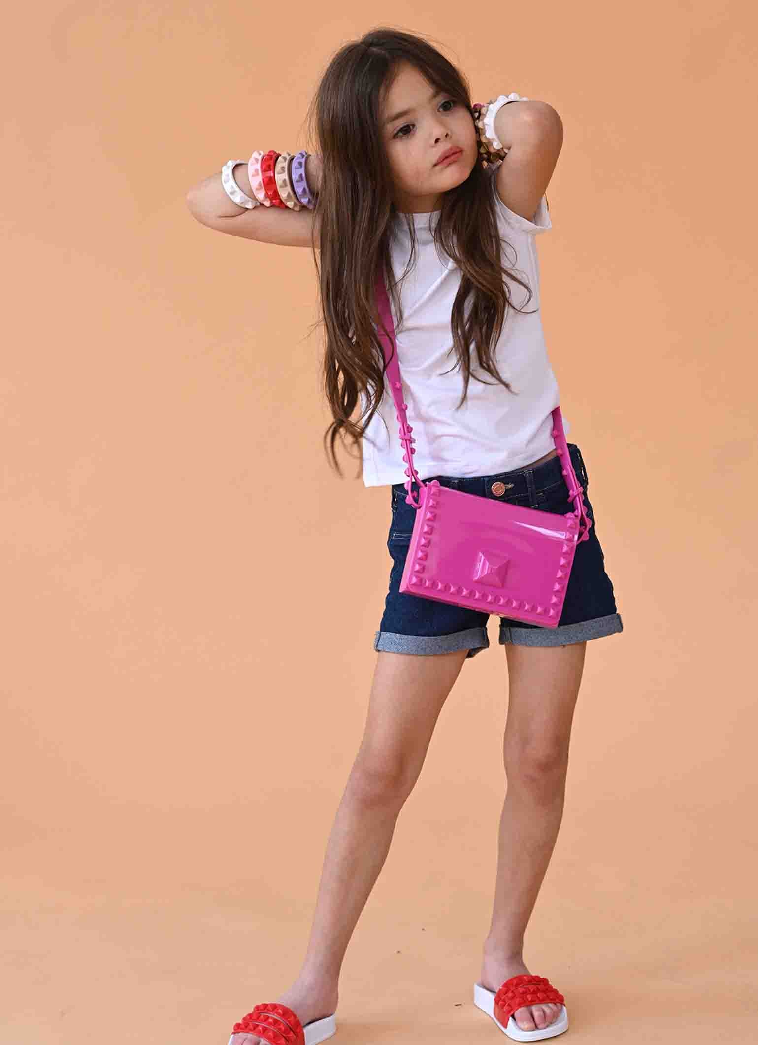 Girl wearing colorful studded jelly bracelets and a bright pink crossbody bag.