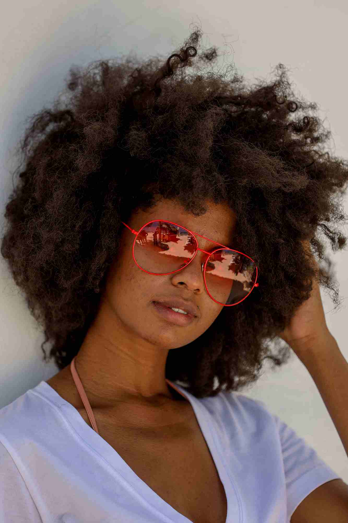 Tropical girl wearing red sunglasses with red lenses and V neck t-shirt in white on the beach