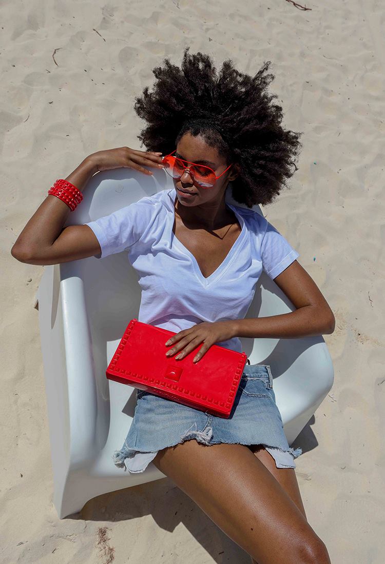 Girl on the beach wearing red sunglasses with red lenses and red jelly bracelets and red jelly bag