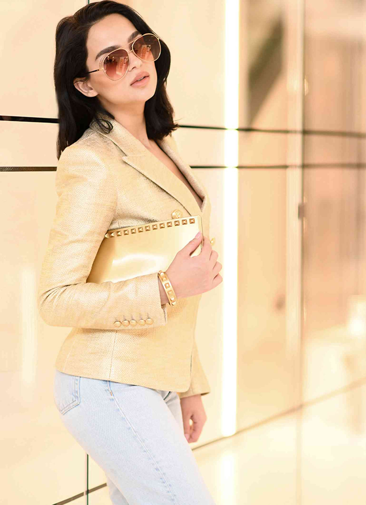 Women wearing a gold color bag with gold bracelets with studs