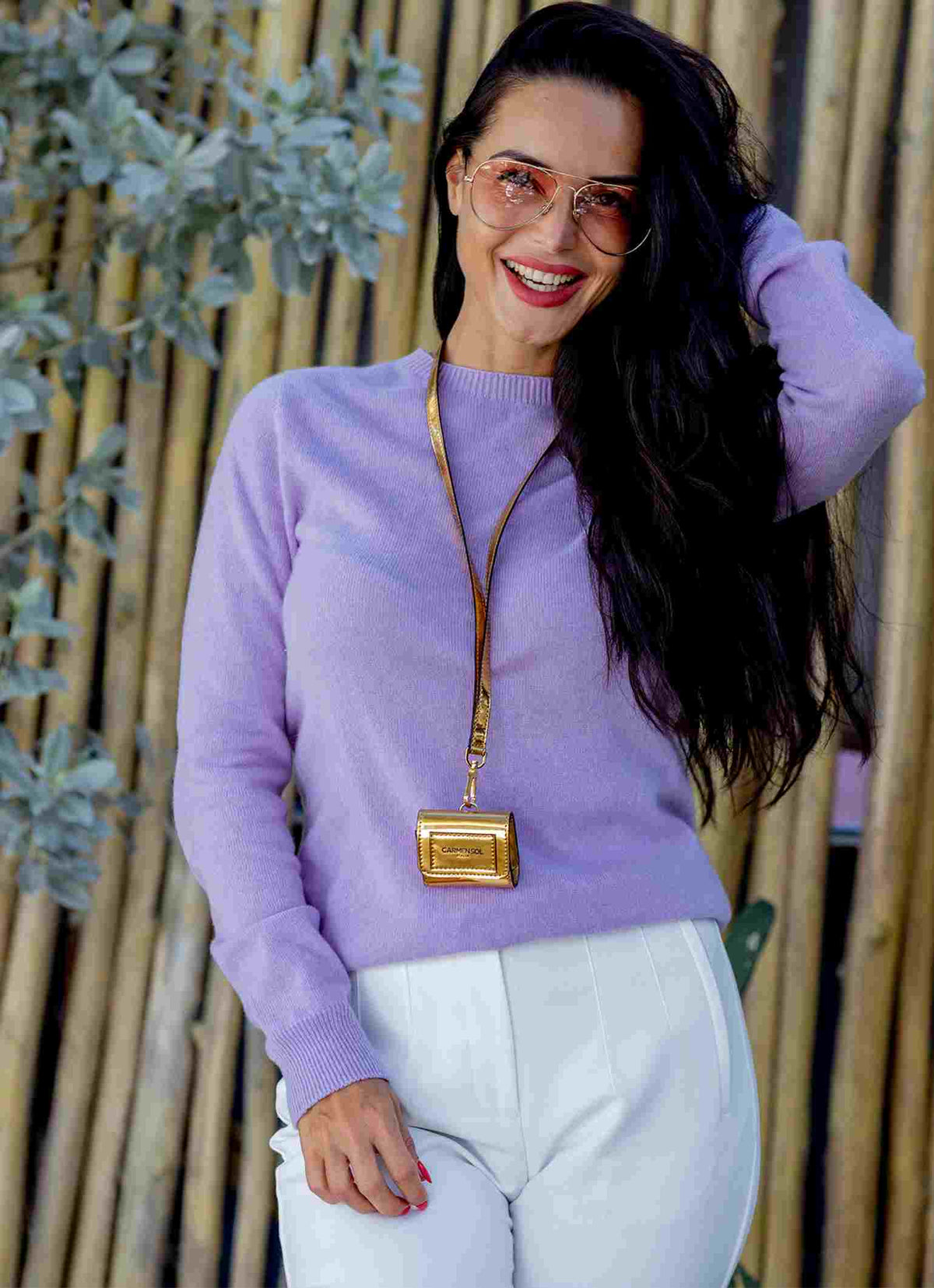 Women wearing handsfree airpod case in color gold along with Carmen Sol cashmere and sunglasses