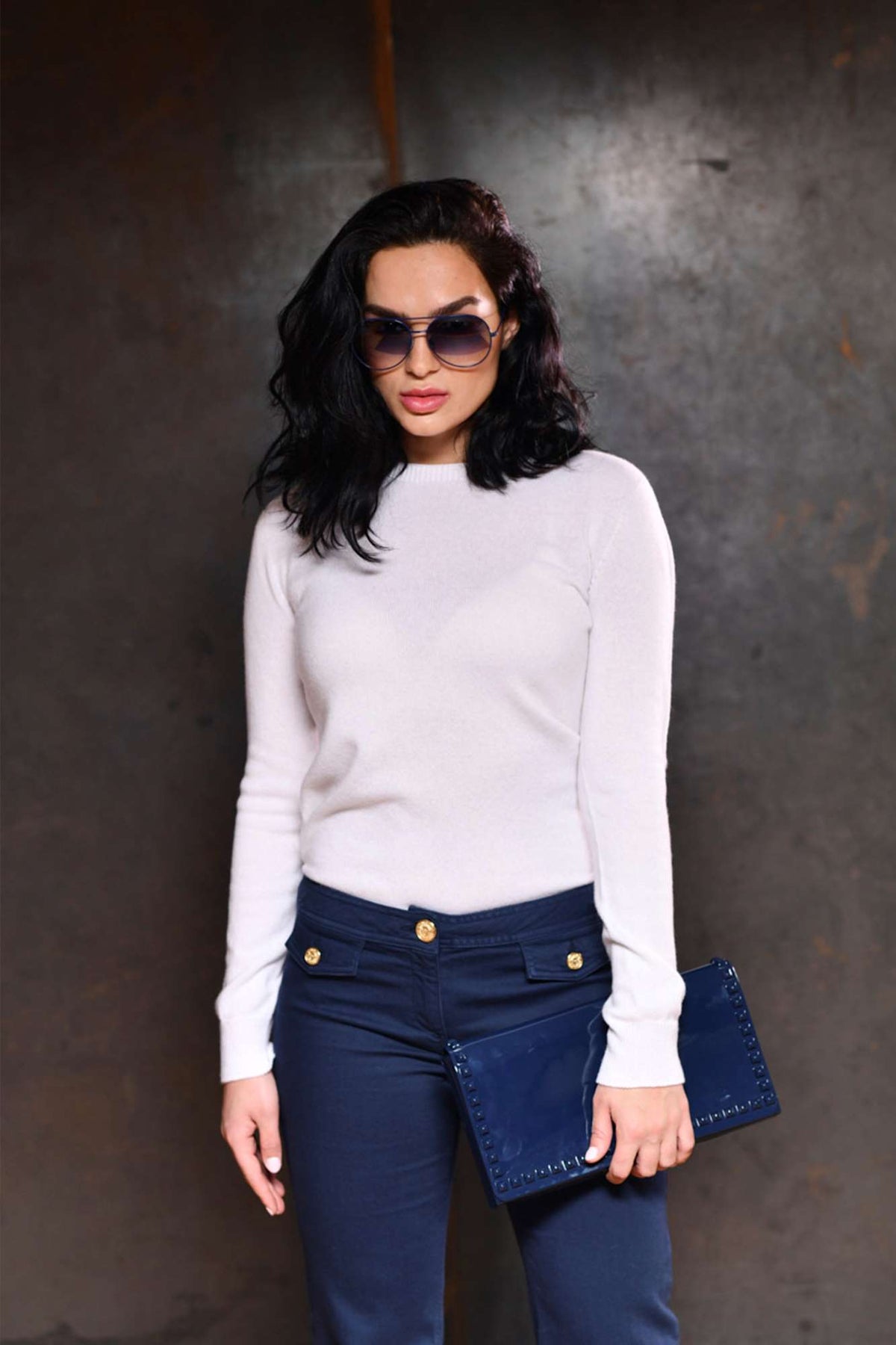 Girl wearing a white cashmere sweater with navy blue aviator sunglasses and jelly purse in navy blue